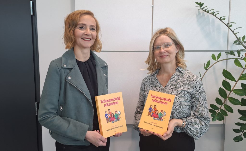 Kuva Camilla Lindholmista ja Leealaura Leskelästä pitelemässä Tutkimusretkellä selkokeileen-kirjoja kädessään