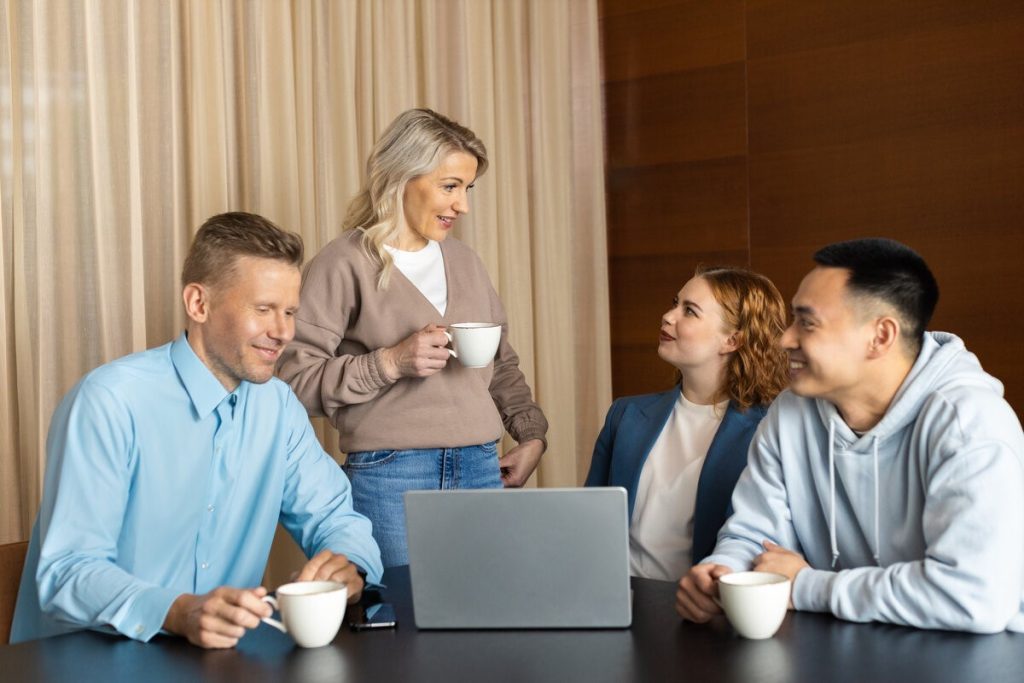 Kaksi miestä ja kaksi naista kerääntyneinä pöydän ympärille neuvotteluhuoneessa. Pöydällä on kannettava tietokone.