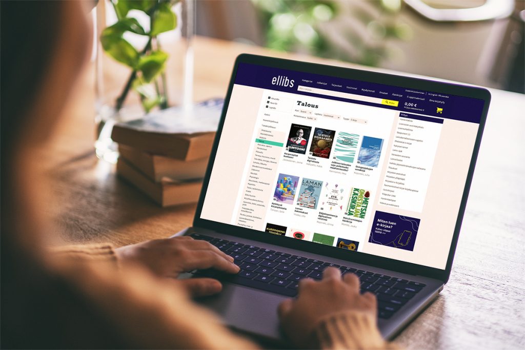 A person is using a laptop with the Ellibs online bookstore open on the screen. In the background, there are books and a green plant on the table.