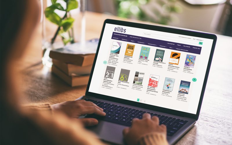 A person using a laptop with the Ellibs e-bookshelf open on the screen, showing a selection of e-books. Books and a green plant are visible on the table in the background.