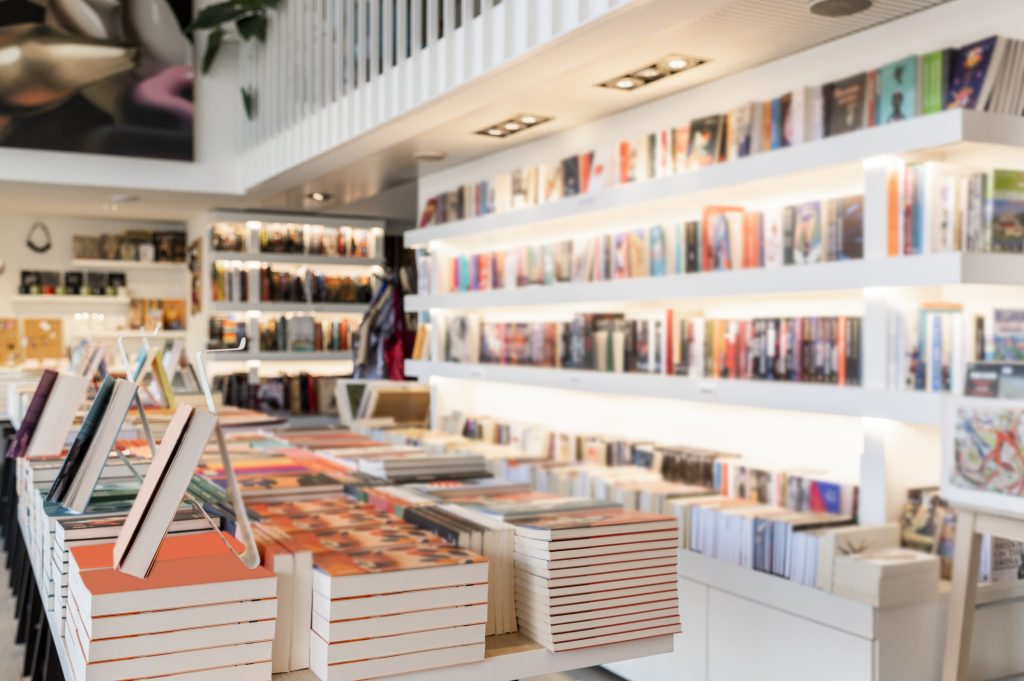 A bright and modern bookstore interior with tables full of stacked books and shelves filled with colorful book covers.